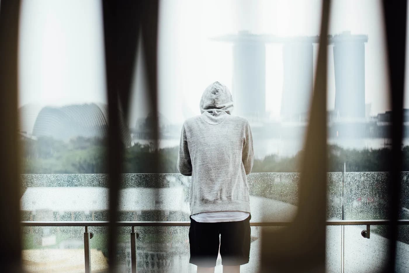 “Person in a hoodie standing on a balcony looking at Singapore landmarks” by chuttersnap on Unsplash
